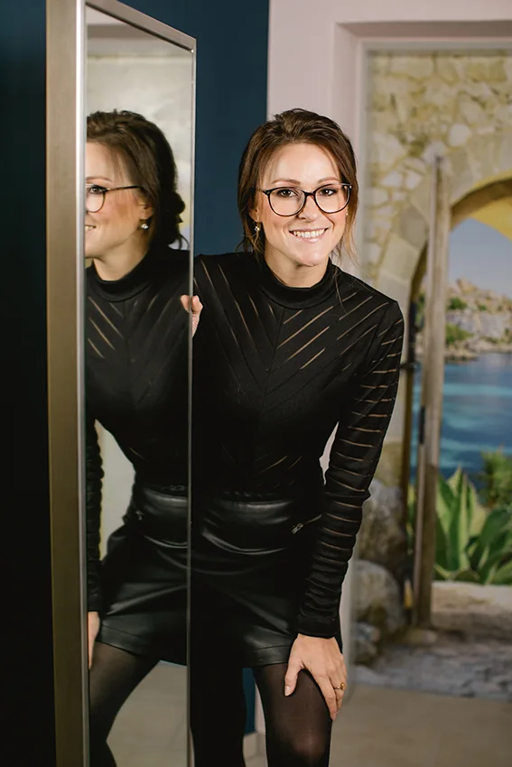 Janine Stelling lächelt neben einem Spiegel in ihrem Atelier