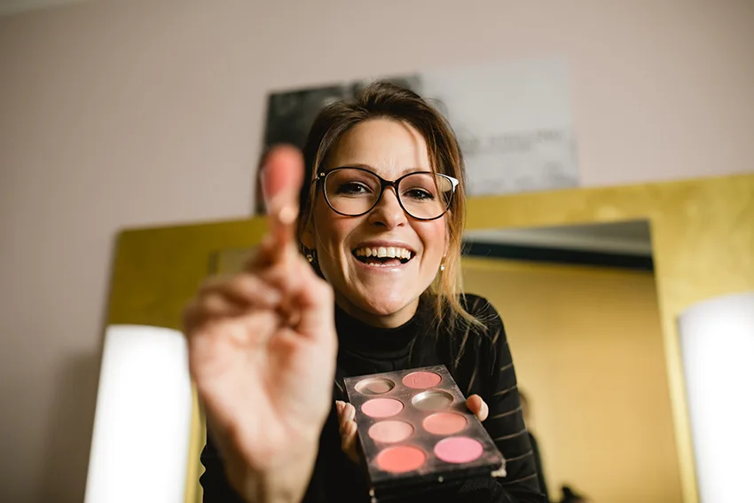 Janine Stelling lächelt mit Make-up-Pinsel und Farbpalette