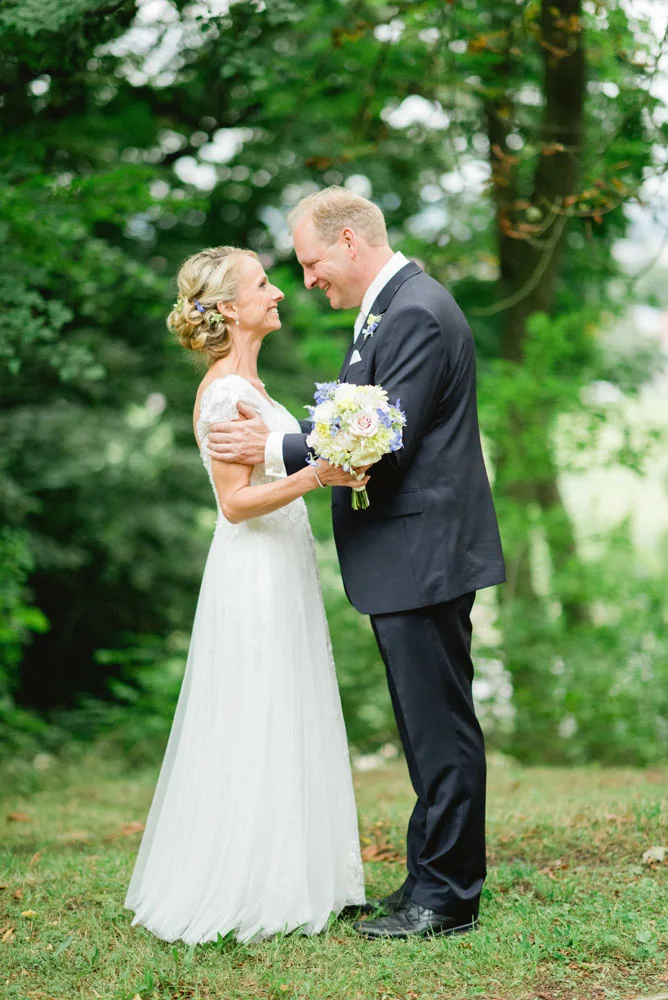 Brautpaar im Garten, die Braut trägt ein Spitzenkleid und einen Blumenstrauß